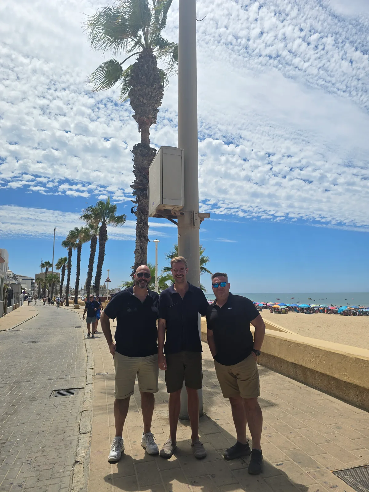 Alex Piatek, Pedro and Francisco Márquez (Paco) at the coastal camera installation on Chipiona’s promenade, with the beach behind them.