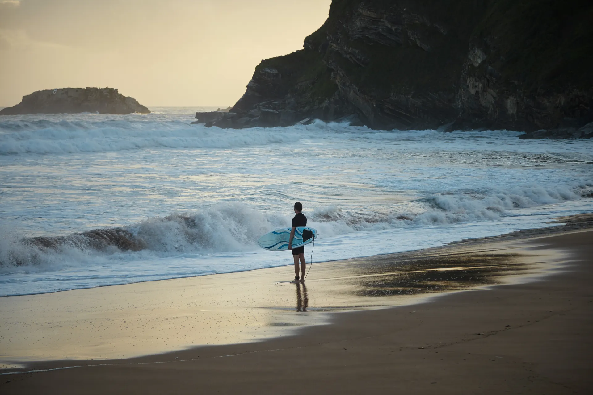 A surfer watching the water from the beach.
